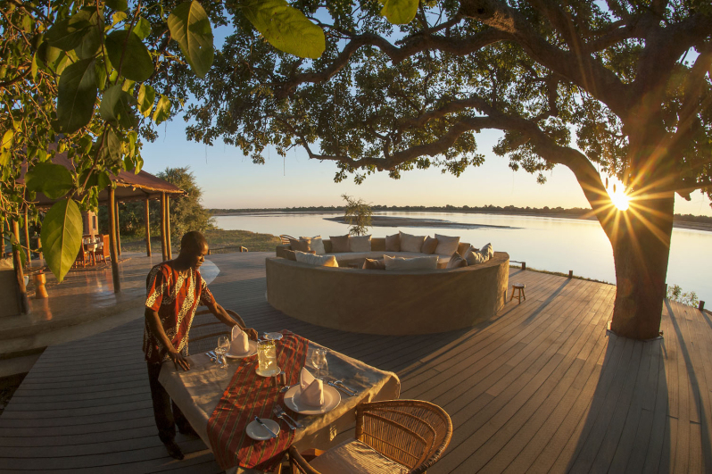 A man setting a table on a wooden deck at sunrise  on the banks of a river