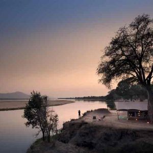 A tent on a river bank with wide views over a floodplain at dusk