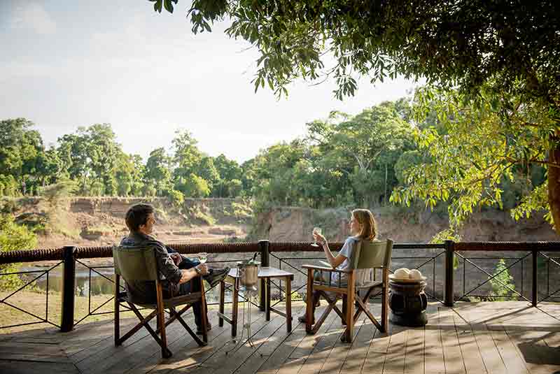 Two people sitting on a deck overlooking the Mara River at Governers Camp